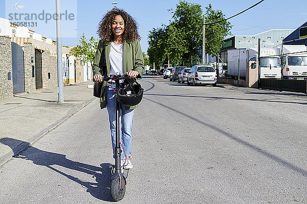 Glückliche Frau fährt elektrischen Roller auf der Straße an einem sonnigen Tag