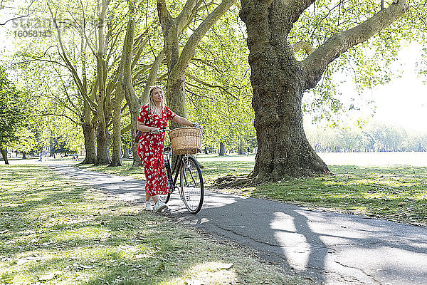 Nachdenkliche Frau mit Fahrrad auf dem Fußweg in einem öffentlichen Park