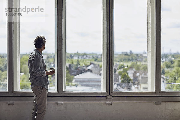 Älterer Mann schaut aus dem Fenster in einer Dachgeschosswohnung