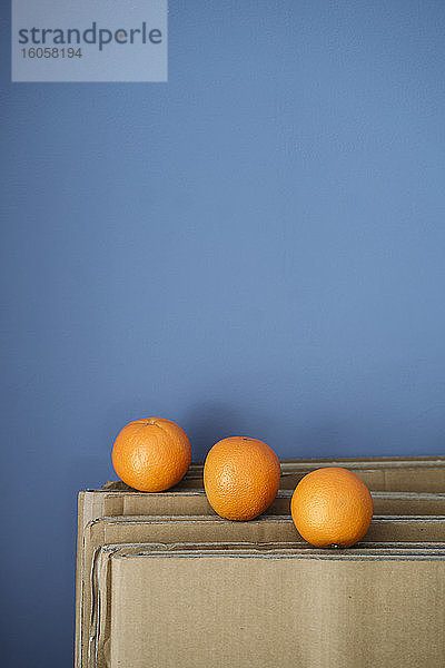Drei Orangen auf Karton gegen blaue Wand