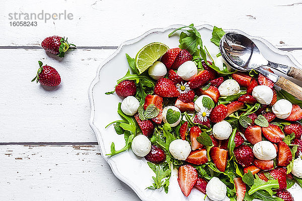 Teller mit vegetarischem Sommersalat mit Limette  Rucola  Erdbeeren  Mozzarella  Minze und Gänseblümchen