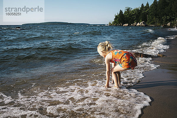 Blondes Mädchen spielt am Ufer des Strandes