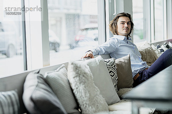 Selbstbewusster Geschäftsmann entspannt sich auf dem Sofa am Fenster eines Cafés