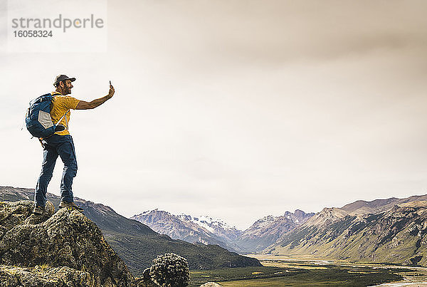 Älterer Mann  der ein Selfie mit seinem Smartphone macht  während er auf einem Felsen gegen den Himmel steht  Patagonien  Argentinien