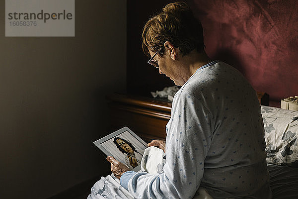 Ältere Frau im Schlafzimmer bespricht sich per Videoanruf mit einem Arzt zu Hause