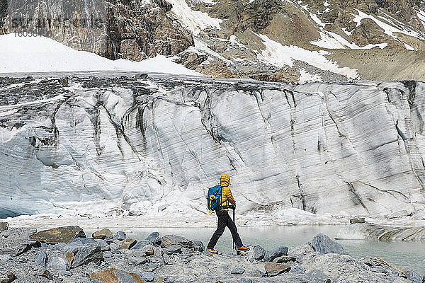 Männlicher Wanderer  der auf Felsen stehend den schmelzenden Gletscher erkundet