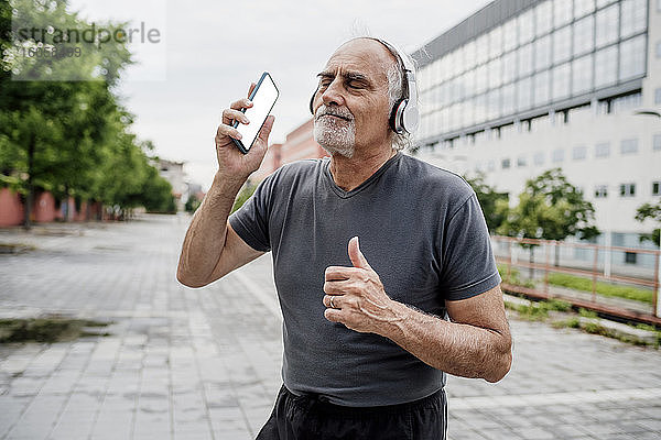 Ältere Frau mit geschlossenen Augen hört Musik  während sie auf einem Fußweg in der Stadt steht