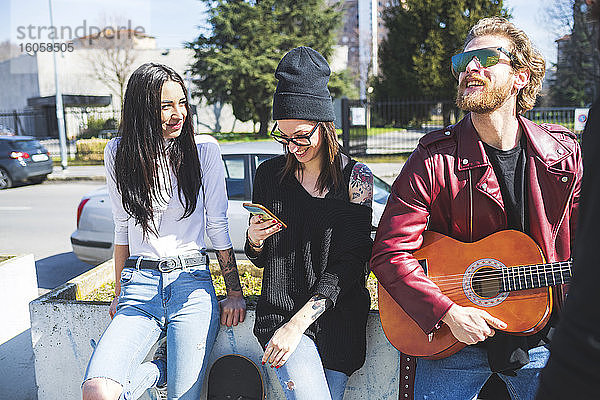 Bärtiger Mann spielt Gitarre  während er mit weiblichen Freunden in der Stadt steht