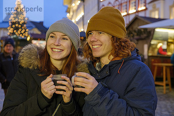 Glückliches junges Paar mit Kaffeetassen auf dem Weihnachtsmarkt