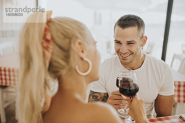 Glückliches junges Paar stößt im Restaurant mit Weingläsern an