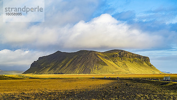 Ein zerklüfteter  mit grüner Tundra bedeckter Felsvorsprung mit einer Straße  die durch die weite Landschaft führt; Island
