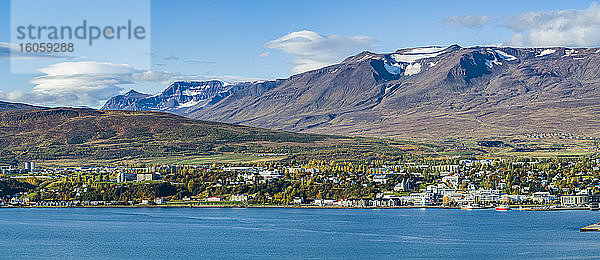 Stadt in Island mit strahlend blauem Wasser und Bergen mit Schneespuren auf den Gipfeln; Island