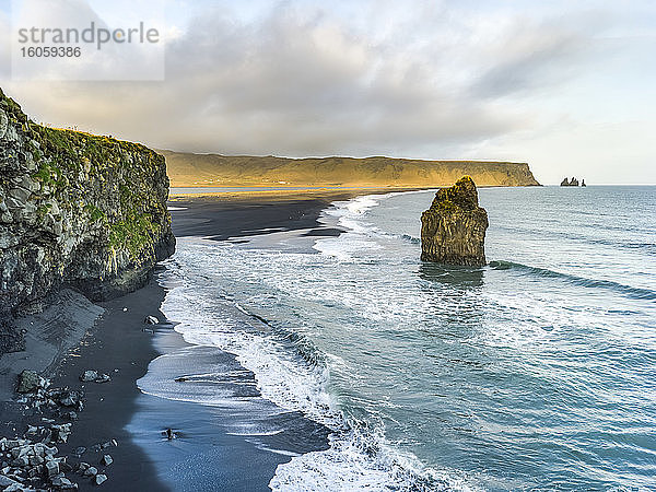 Klippen und eine Felsformation entlang der Küstenlinie der südlichen Region Islands  mit der Brandung  die auf schwarzen Sand gespült wird  im Vordergrund; Myrdalshreppur  südliche Region  Island