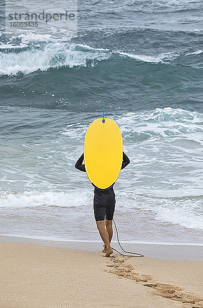 Ein männlicher Surfer geht am Strand mit einem leuchtend gelben Surfbrett in Richtung Wasser; Kihei  Maui  Hawaii  Vereinigte Staaten von Amerika