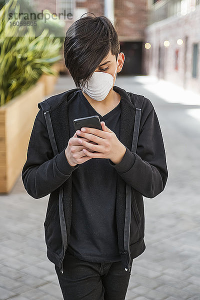 Zwischenmensch  der während der Coronavirus-Weltpandemie sein Smartphone benutzt und eine Schutzmaske zum Schutz vor COVID-19 trägt; Toronto  Ontario  Kanada