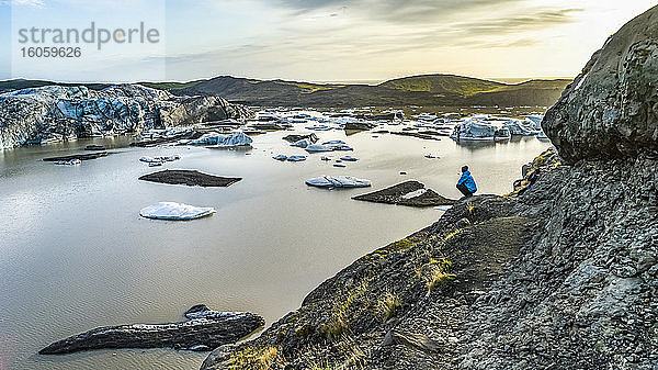 Ein Mann kauert auf einem felsigen Abhang  um in der Dämmerung auf den Svinafellsjokull-Gletscher zu blicken; Hornafjordur  östliche Region  Island