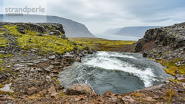 Ein Fluss fließt durch eine zerklüftete Landschaft in einen Fjord; Westfjorde  Island