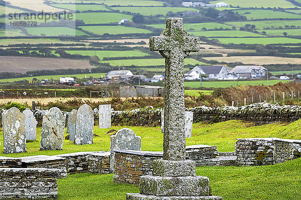 Alter Steinkreuz-Grabstein auf dem Friedhof mit einem Flickenteppich von Feldern im Hintergrund; Grafschaft Cornwall  England