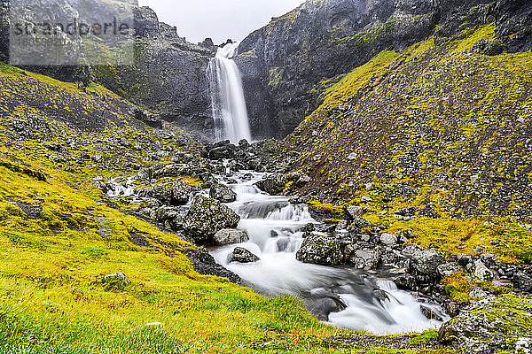 Ein Wasserfall über einer felsigen Landschaft mit einem Fluss  der sich über die Felsen ergießt; Djupivogur  östliche Region  Island