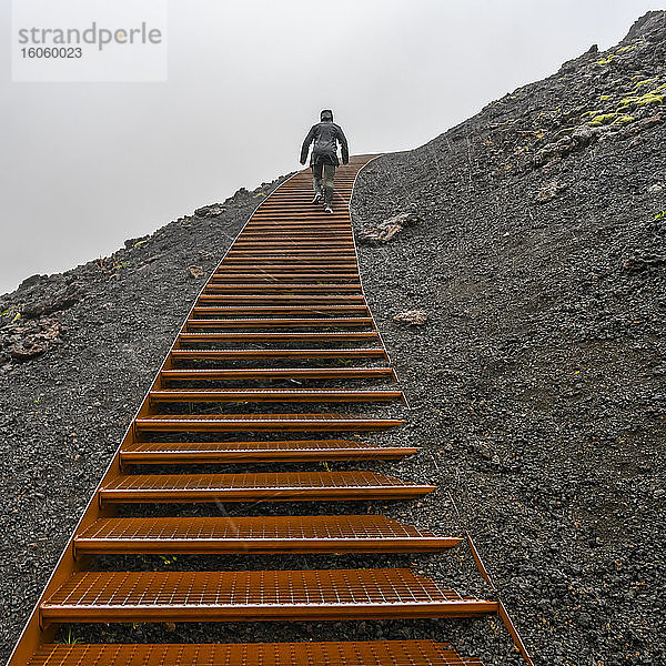 Im Regen auf Metallstufen im Vulkangestein klettern; Snaefellsbaer  Westliche Region  Island