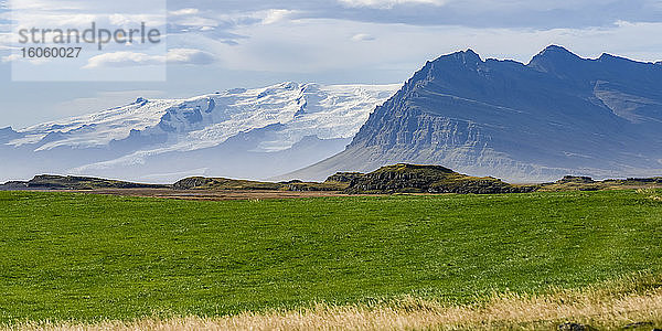 Landschaft im Südosten Islands mit zerklüfteten Bergen und Grasfeldern und schneebedeckten Bergen in der Ferne; Hornafjorour  östliche Region  Island