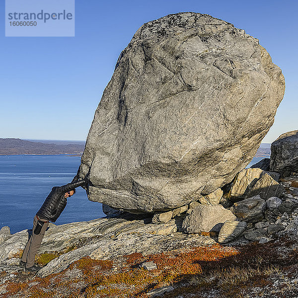 Mann steht mit den Händen auf einem großen Felsblock  was das Bild der Stärke vermittelt; Sermersooq  Grönland