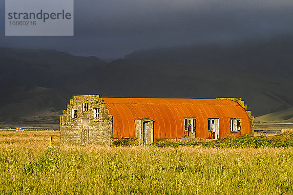 Orangefarbene Quonset-Hütte als Scheune auf einem Acker; Myrdalshreppur  Südliche Region  Island