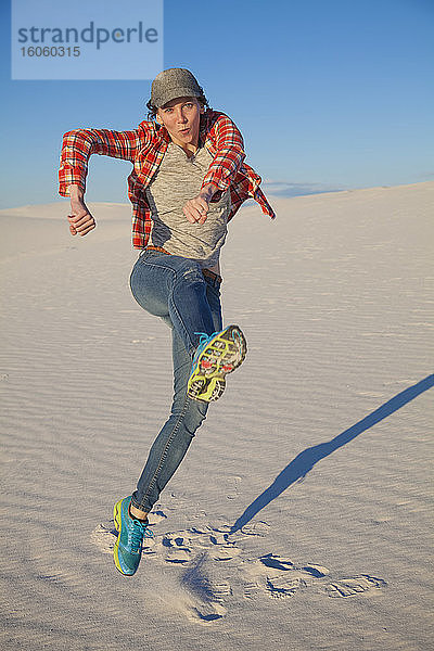 Eine junge Frau springt auf dem weissen Sand mit blauem Himmel in die Luft  White Sands National Monument; Alamogordo  New Mexico  Vereinigte Staaten von Amerika