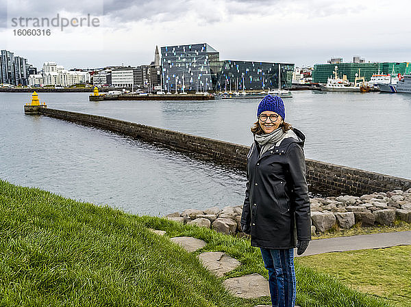 Eine Frau steht an der Uferpromenade mit der Harpa-Konzerthalle und dem Konferenzzentrum im Hintergrund; Rejkjavik  Reykjavik  Island