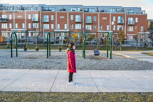 Junges Mädchen steht auf einem Spielplatz und trägt eine Schutzmaske zum Schutz vor COVID-19 während der Coronavirus-Weltpandemie; Toronto  Ontario  Kanada