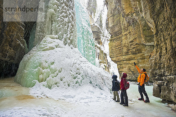 Drei Personen sehen einen großen gefrorenen Canyon-Wasserfall  Jasper National Park; Alberta  Kanada