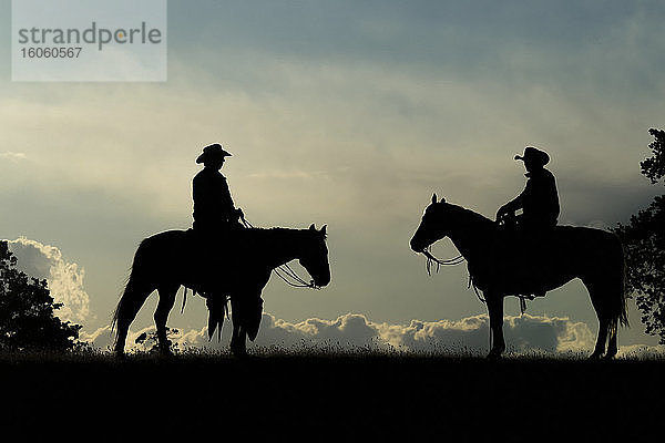 Silhouette von zwei Cowboys auf Pferden vor einem bewölkten Himmel; Montana  Vereinigte Staaten von Amerika