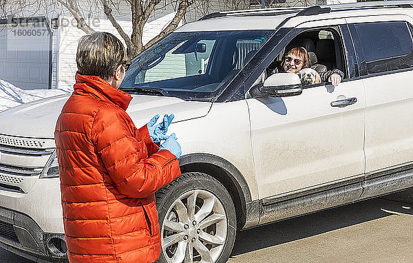 Zwei Frauen treffen sich während der Covid-19-Weltpandemie in der Nachbarschaft  physische Distanzierung mit einer Frau in ihrem Auto und einer Frau auf der Straße; St. Albert  Alberta  Kanada