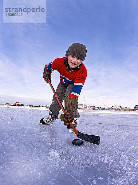 Junge Junge spielt Hockey im Freien auf einer gefrorenen Eisbahn; Alberta  Kanada