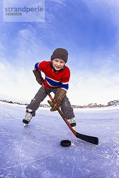 Junge Junge spielt Hockey im Freien auf einer gefrorenen Eisbahn; Alberta  Kanada