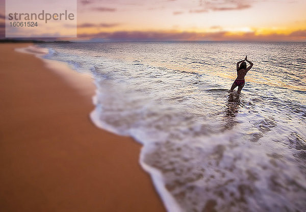 Ein verschwommenes Bild einer Frau  die in der Brandung steht und auf den Sonnenuntergang am zwei Meilen langen und dreihundert Fuß breiten Papohaku-Strand am Westufer von Molokai schaut. Dies ist der längste weisse Sandstrand auf den Hawaii-Inseln; Molokai  Hawaii  Vereinigte Staaten von Amerika