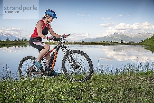 Mountainbikerin  Ende vierzig fährt mit E-Bike am Seeufer vor Bergkulisse  Mutterer Alm  Stubaier Alpen  Mutters  Tirol  Österreich  Europa
