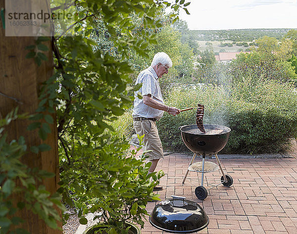 älterer Mann grillt Rippen auf der vorderen Veranda