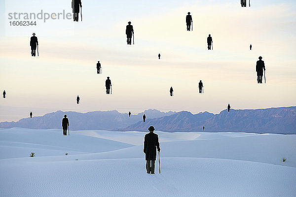 Männer mit Melonenmützen und Regenschirm Umrisse von Figuren  die über der Erde in einer Sanddünenwüste schweben