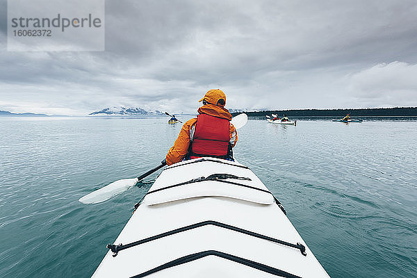Eine Person  die in einem Doppel-Seekajak auf ruhigem Wasser vor der Küste Alaskas paddelt.