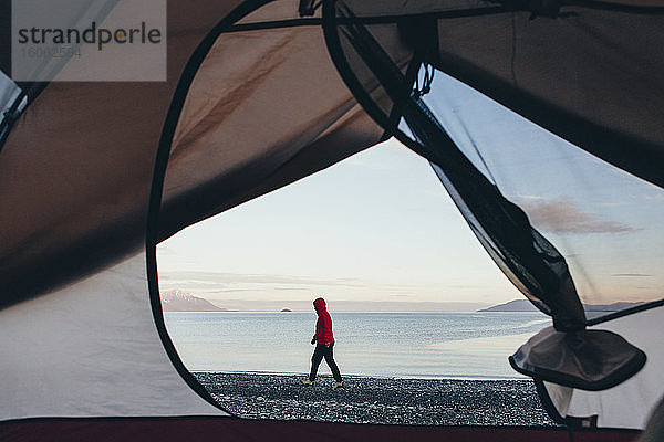 Blick durch die Tür des Campingzeltes einer Frau  die am Strand Muir Inlet in der Ferne spazieren geht Glacier Bay National Park Alaska