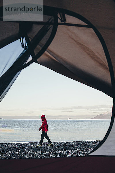 Blick durch die Tür des Campingzeltes einer Frau  die am Strand Muir Inlet in der Ferne spazieren geht Glacier Bay National Park Alaska