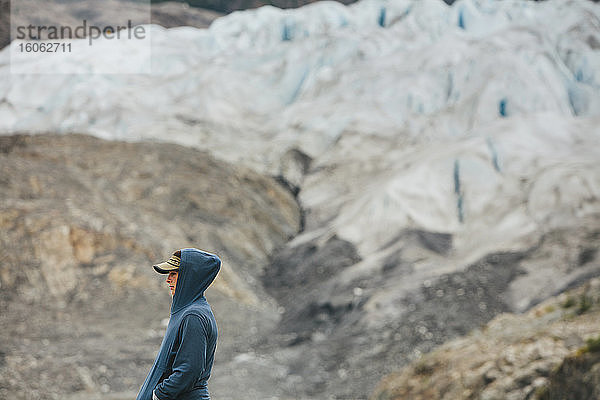 Eine junge Frau  die am Ende eines Gletschers an einer felsigen Küste in Alaska steht.