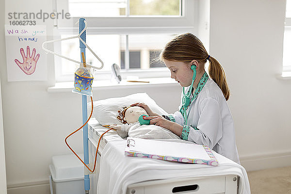 Junges  als Ärztin verkleidetes Mädchen  das vorgibt  eine Patientin in einem unechten Krankenhausbett zu behandeln