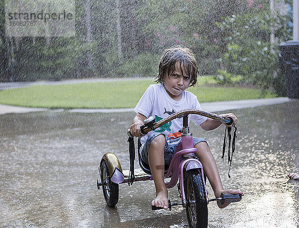 5 Jahre alter Junge fährt mit seinem Dreirad im Regen