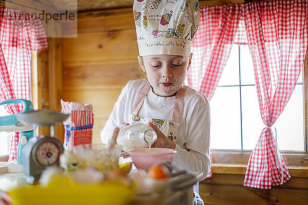 Junges Mädchen im Wendy-Haus gießt Milch ein und gibt vor  in der Küche zu kochen