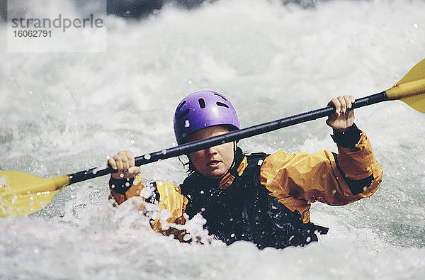 Weibliche Wildwasser-Kajakfahrerin  die Stromschnellen paddelt und auf einem schnell fließenden Fluss surft.