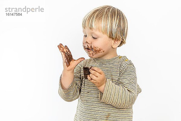 Süßes blondes Kleinkind isst mit großer Freude Schokoladentafel  weißer Hintergrund  Polen  Europa