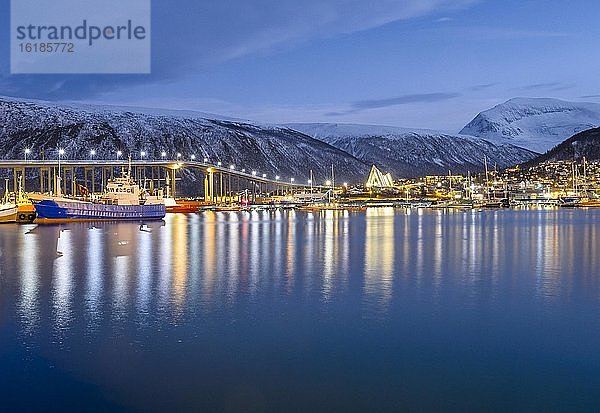 Blick über den Hafen und Stadt mit Tromsøbrua oder Tromsø-Brücke  hinten Tromsdalen Kirche  Eismeerkathedrale  Ishavskatedralen  in der Dämmerung  Polarnacht  Winter  Tromsö  Troms  Norwegen  Europa