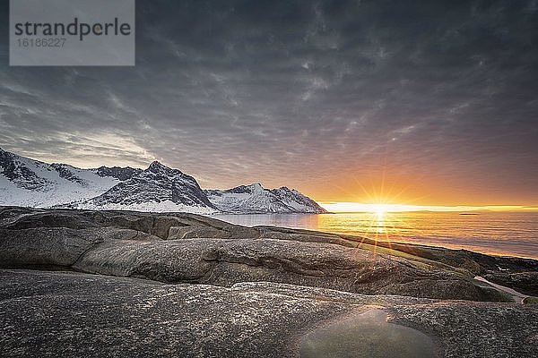 Felsstrand von Tungeneset  schneebedeckte Berggipfel im warmen Sonnenlicht über dem Meer  Steinfjorden  Insel Senja  Skaland  Troms  Norwegen  Europa